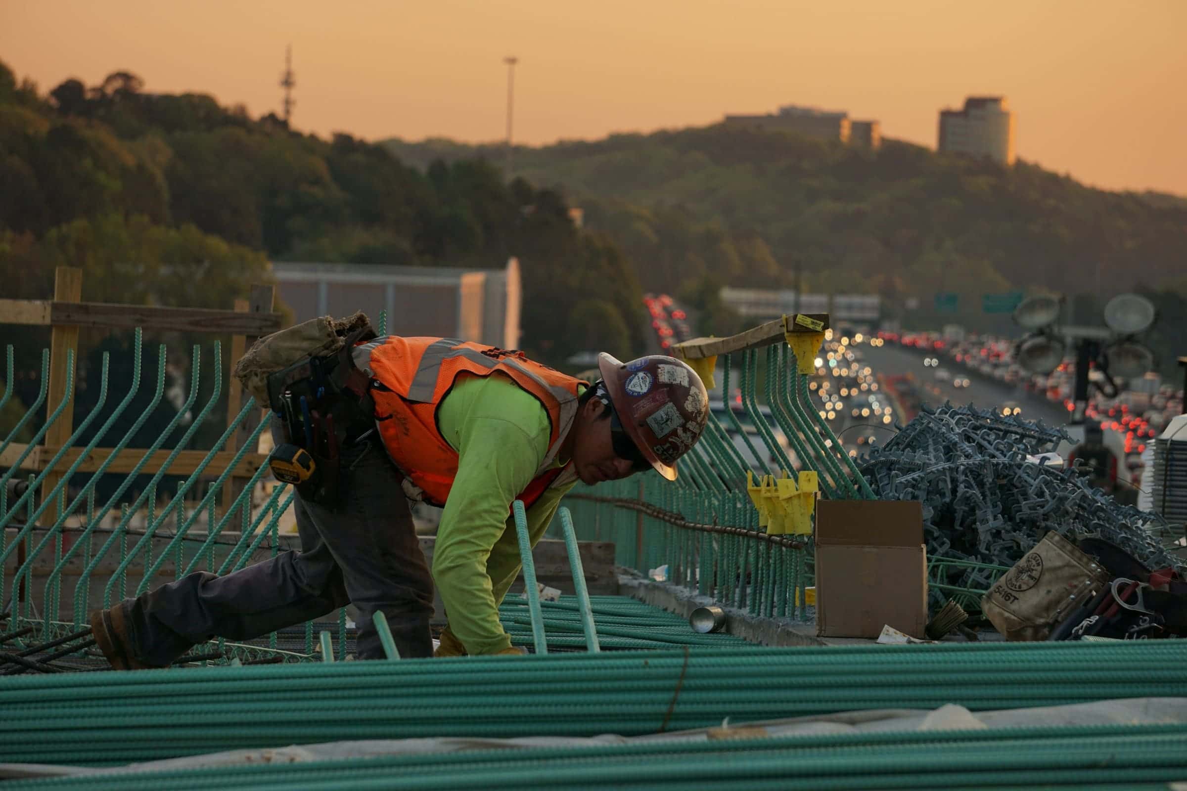 Worker in high-visibility gear fastening metal roof panels on a commercial structure